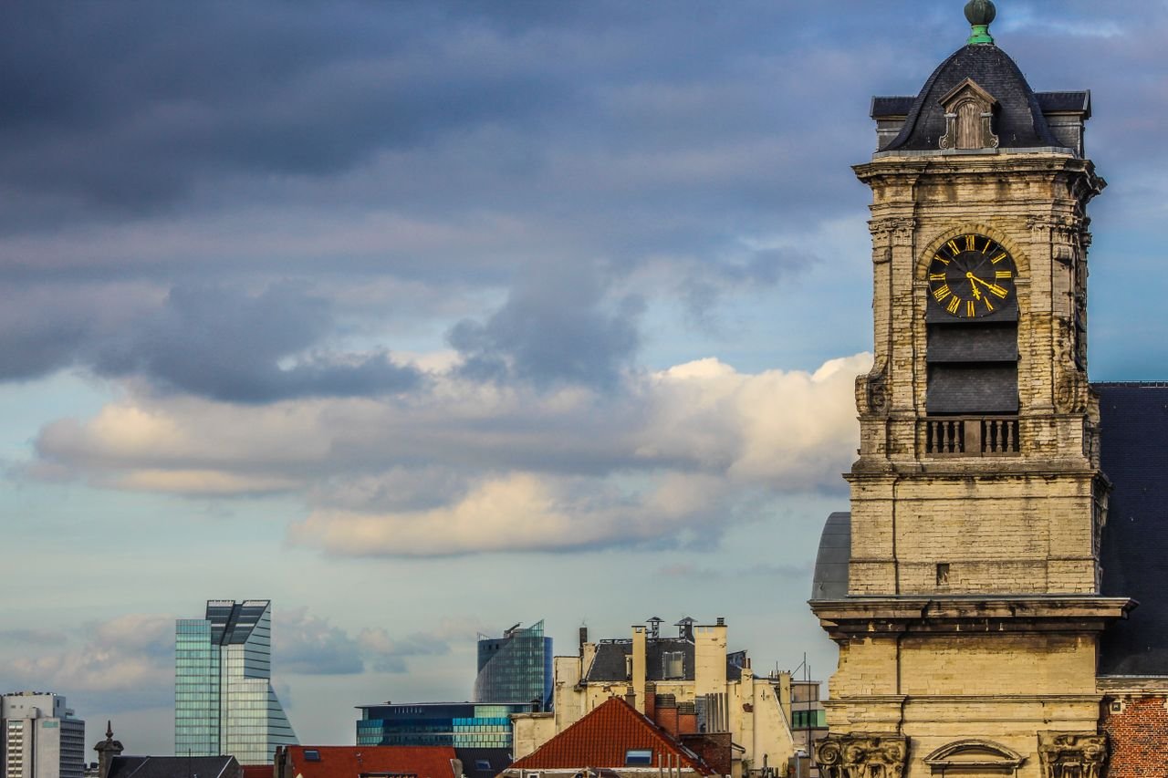Historic clock tower against urban skyline under cloudy sky. Captivating blend of old and new architecture.